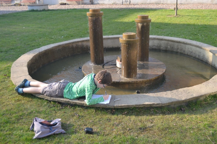 Schulkind lieg am Brunnen im Rittergut Limbach und schreibt in sein Heft